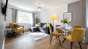 A modern living room with a sofa, yellow chairs, a dining table, and a TV mounted on the wall.