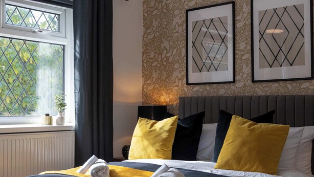 A hotel room with a bed, a window with curtains, a radiator, and framed artwork on the wall.