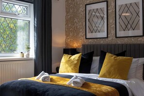 A hotel room with a bed, a window with curtains, a radiator, and framed artwork on the wall. - Spacious Apartment Near MCR Airport (Manchester)