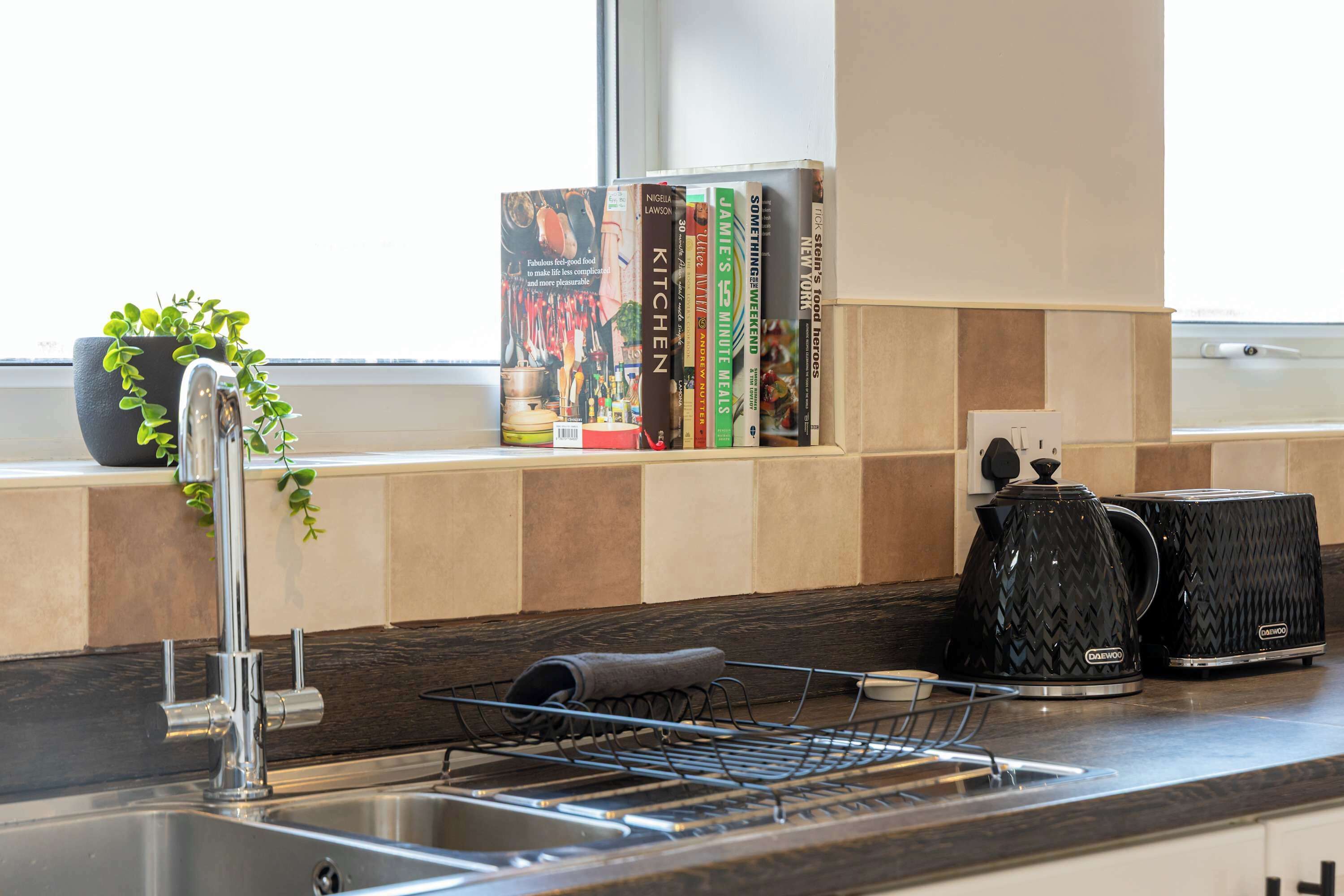 Una cocina con un grifo moderno, hervidor, tostadora y una estantería llena de libros de cocina.