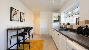 A modern kitchen with a dining area, white cabinetry, a black countertop, and a yellow rug.