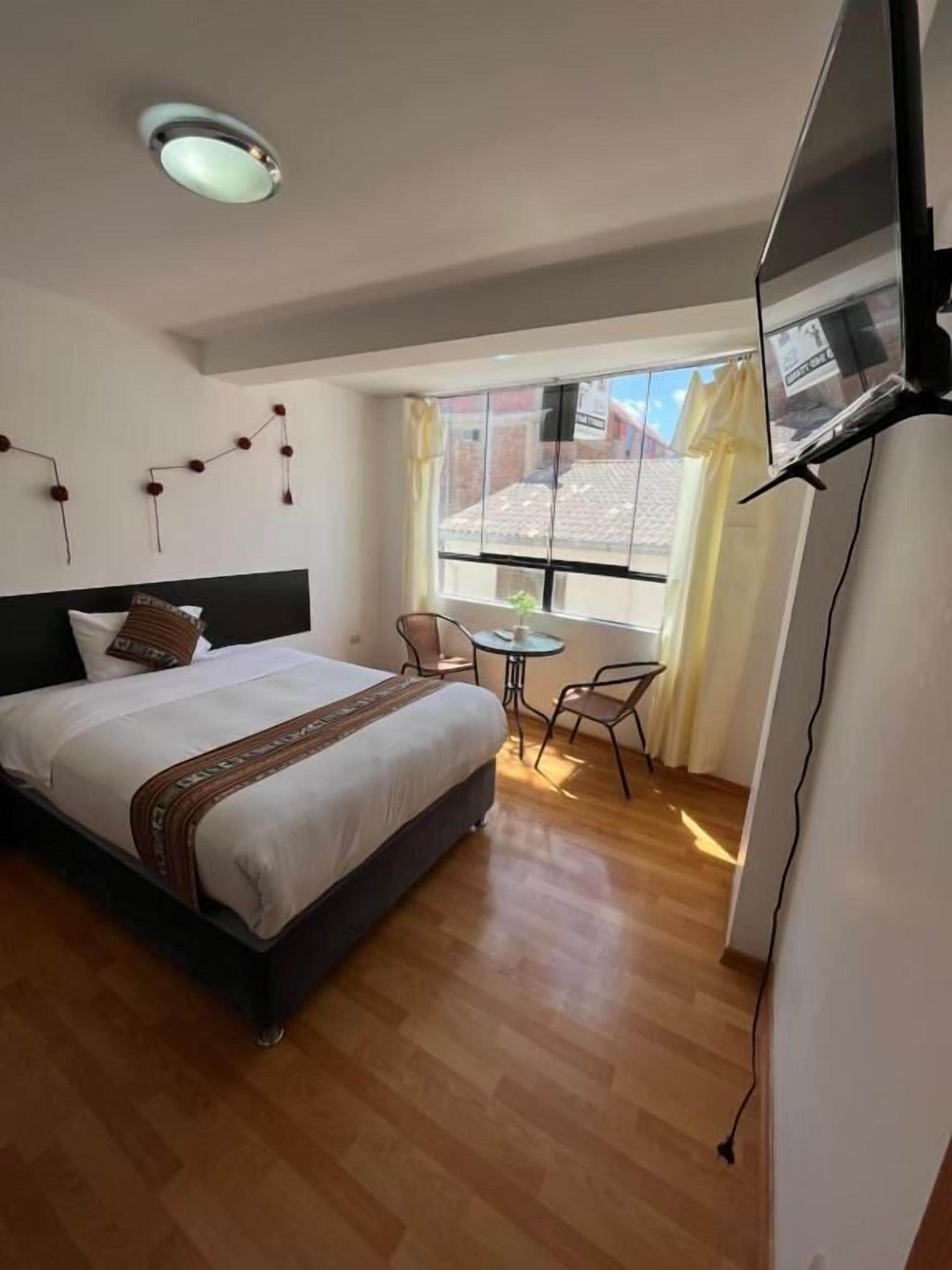 Habitación de hotel con cama, una mesita, una silla, televisión y ventana con cortinas.