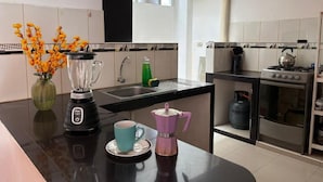 Et moderne køkken med en sort bordplade, kaffemaskine, blender og elkedel.