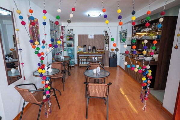 A dining area with round tables and wicker chairs, a wooden counter with a coffee machine, and colorful hanging decorations. - PERUMANTA HOTEL BOUTIQUE (Cusco)