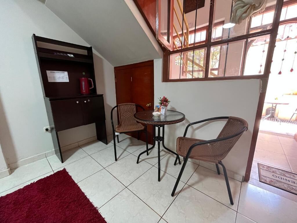 A small room with a red rug, two wicker chairs, a small table, and a window with a view of the outside.