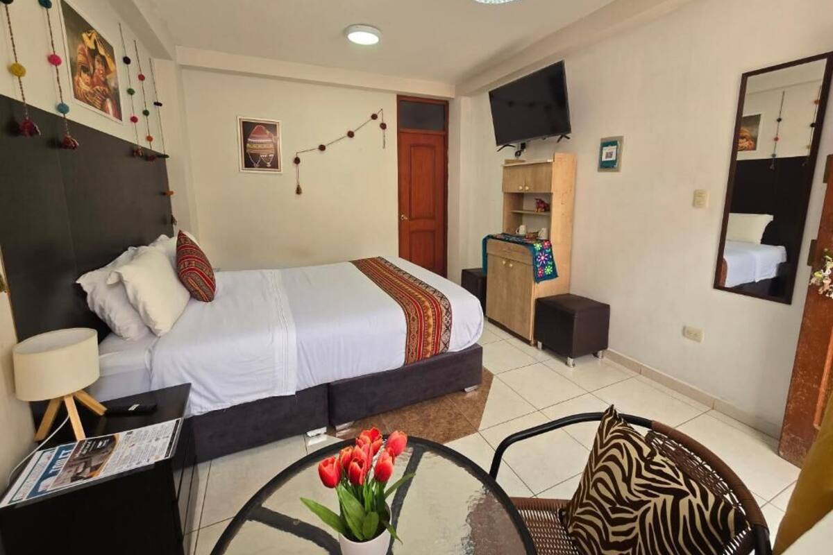 A hotel room with a bed, a desk with a lamp, a chair, a TV, and a mirror.