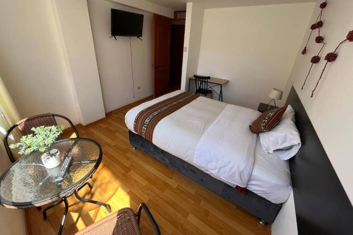 A bedroom with a bed, a TV, a small table with chairs, and a potted plant.