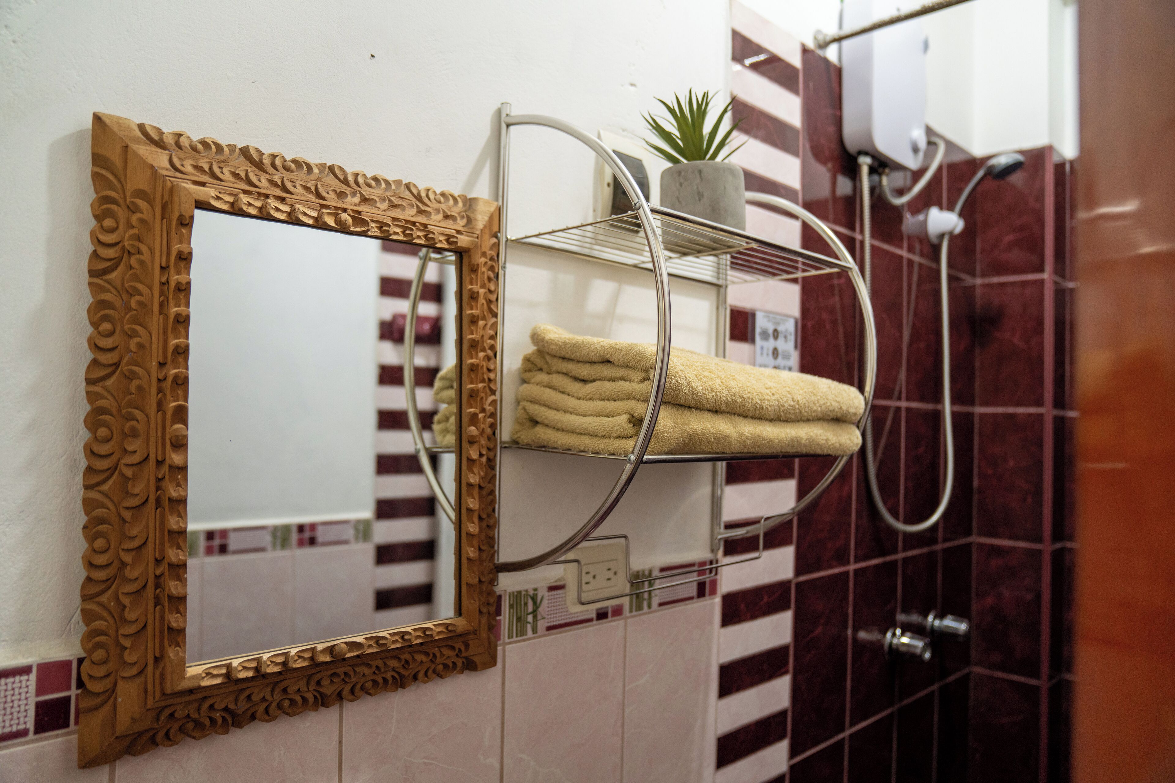 A bathroom with a decorative mirror, a towel rack with folded towels, a potted plant, and a shower area.