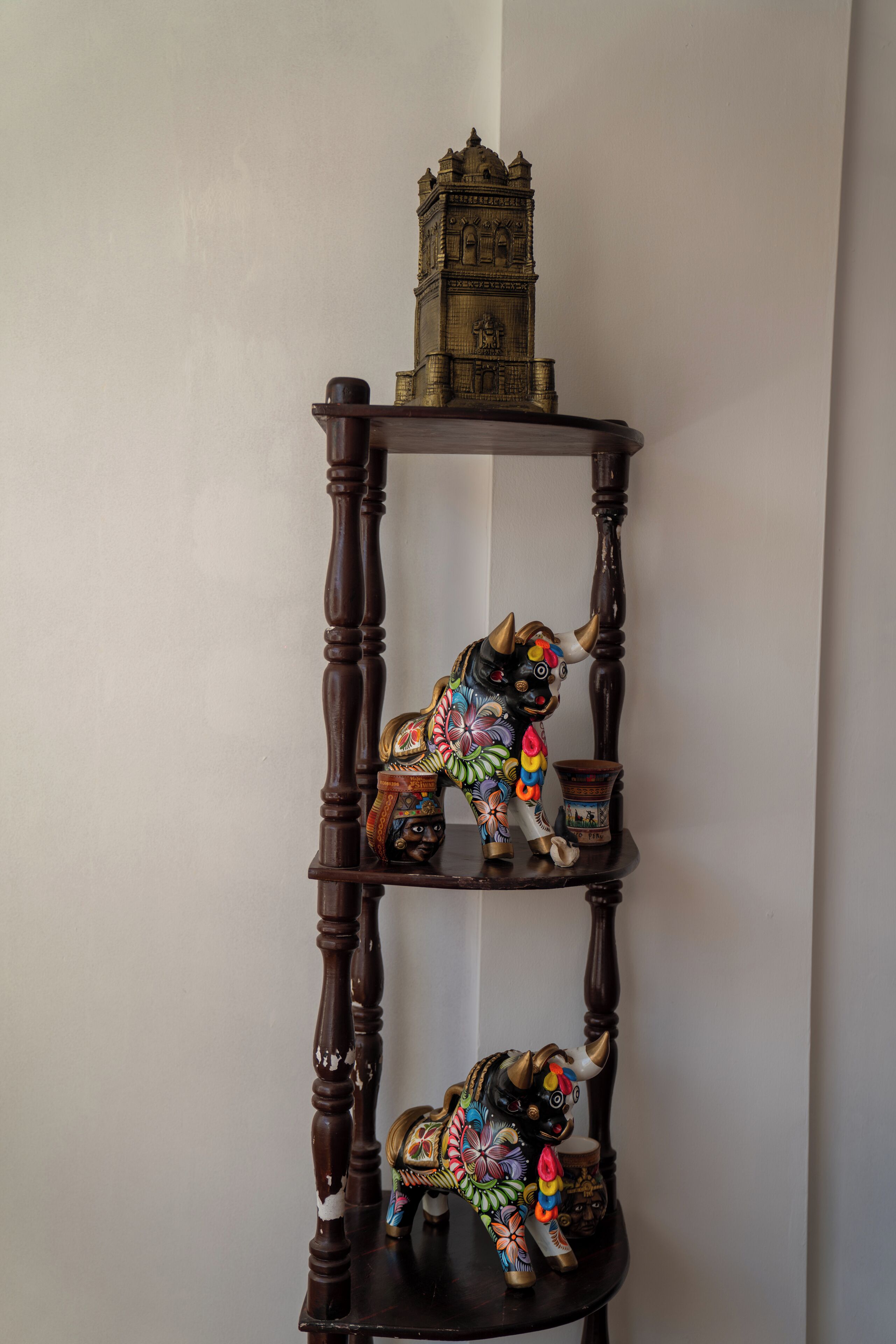 A wooden three-tiered shelf with a decorative clock on top, a colorful painted bull on the middle tier, and a smaller figure on the bottom tier.