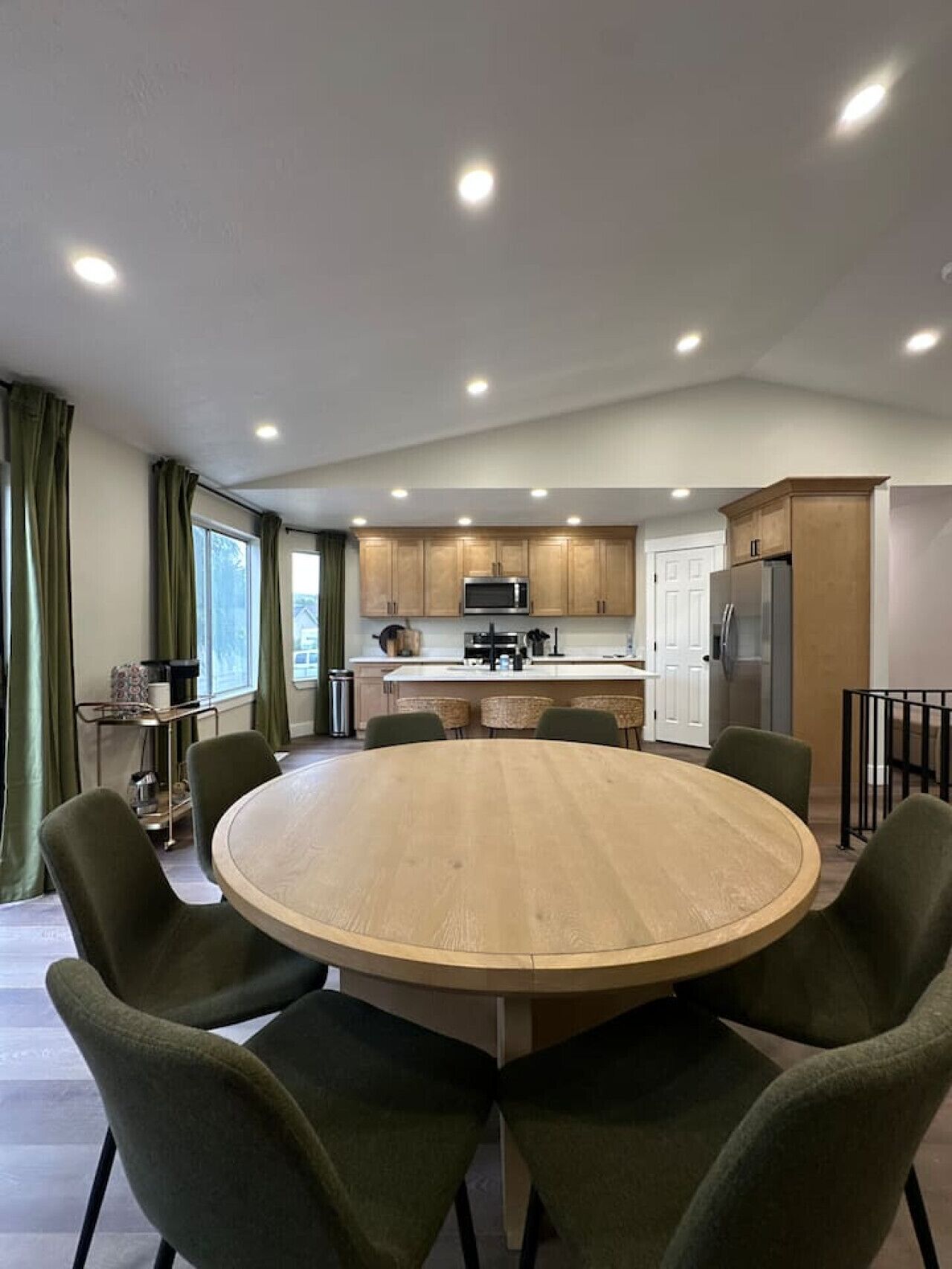 A modern kitchen with a central island, wooden cabinets, and a stainless steel refrigerator.