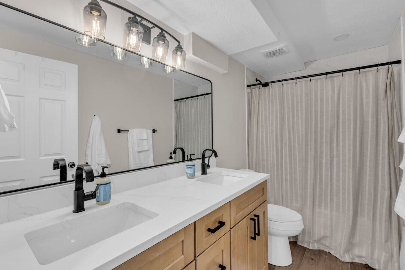 Une salle de bain moderne avec un grand miroir, deux vasques, des toilettes et un rideau de douche.