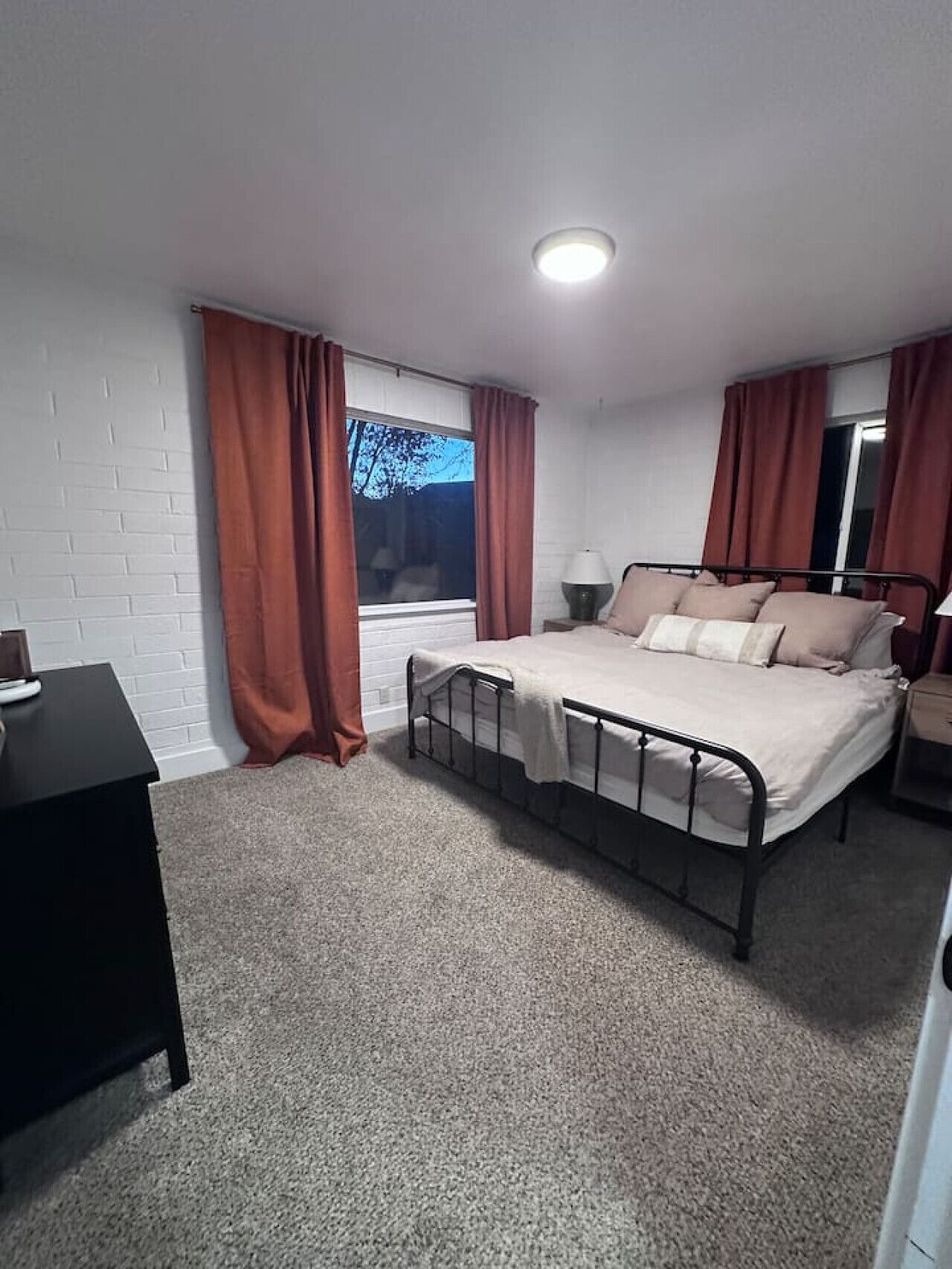 Une chambre à coucher avec un lit, une table de chevet, un bureau et une fenêtre avec des rideaux.