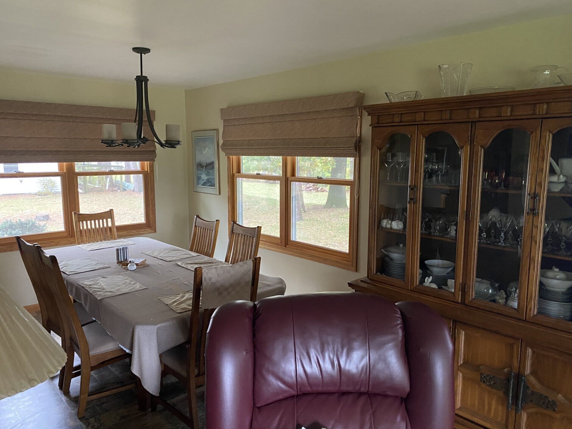 Une salle à manger avec une table dressée pour quatre personnes, des chaises en bois, un fauteuil en cuir et un buffet.
