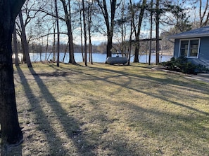 A residential area with a grassy lawn, trees, a house, and a body of water in the background.