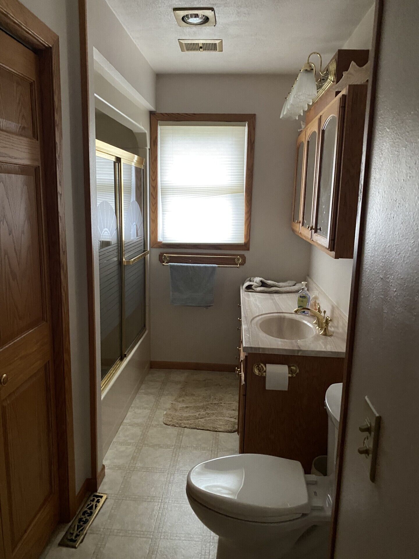 A bathroom with a toilet, sink, vanity, and a window with blinds.