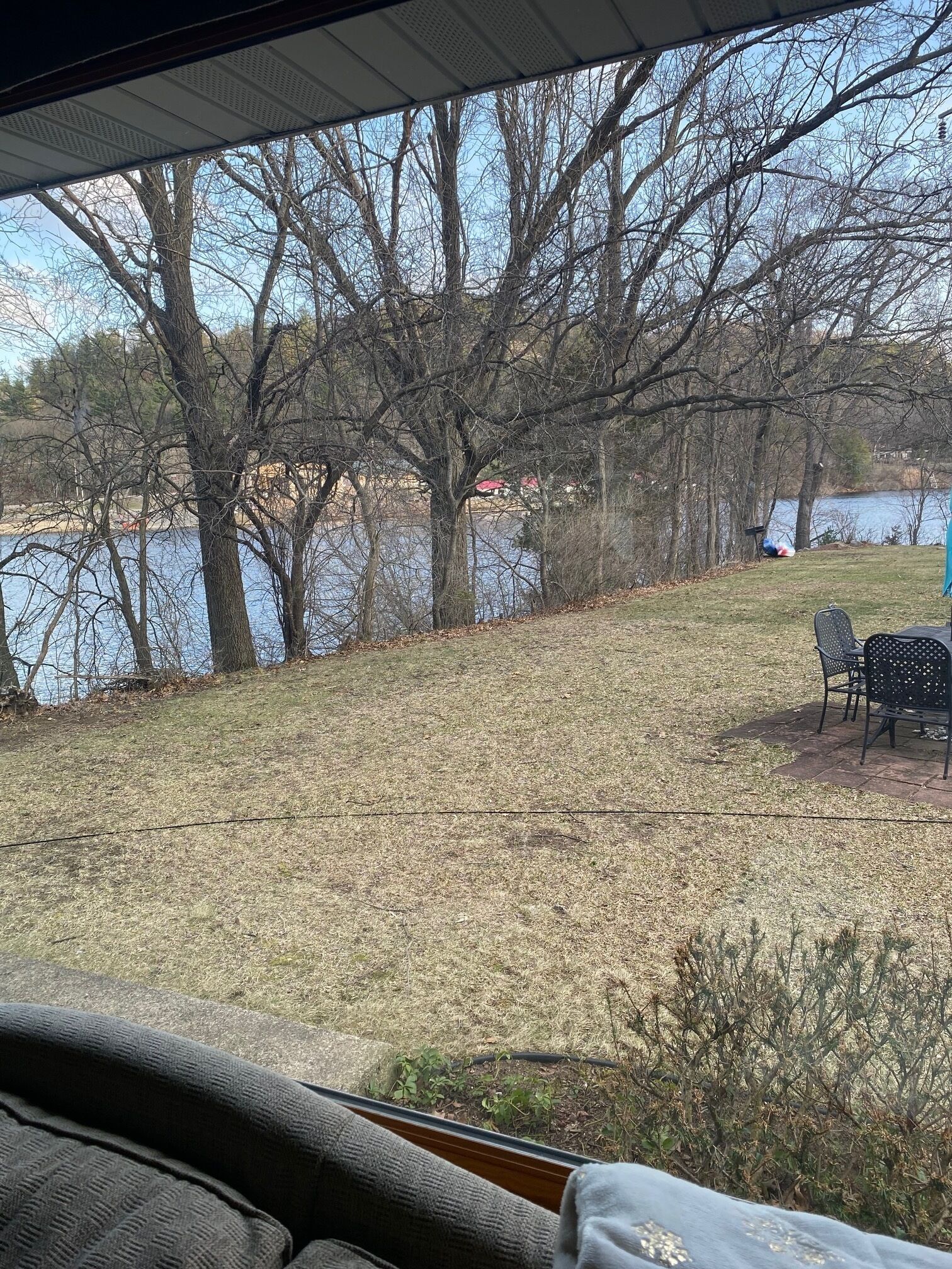 A view from inside a vehicle looking out at a grassy area with trees and a body of water. There are chairs and a table visible.
