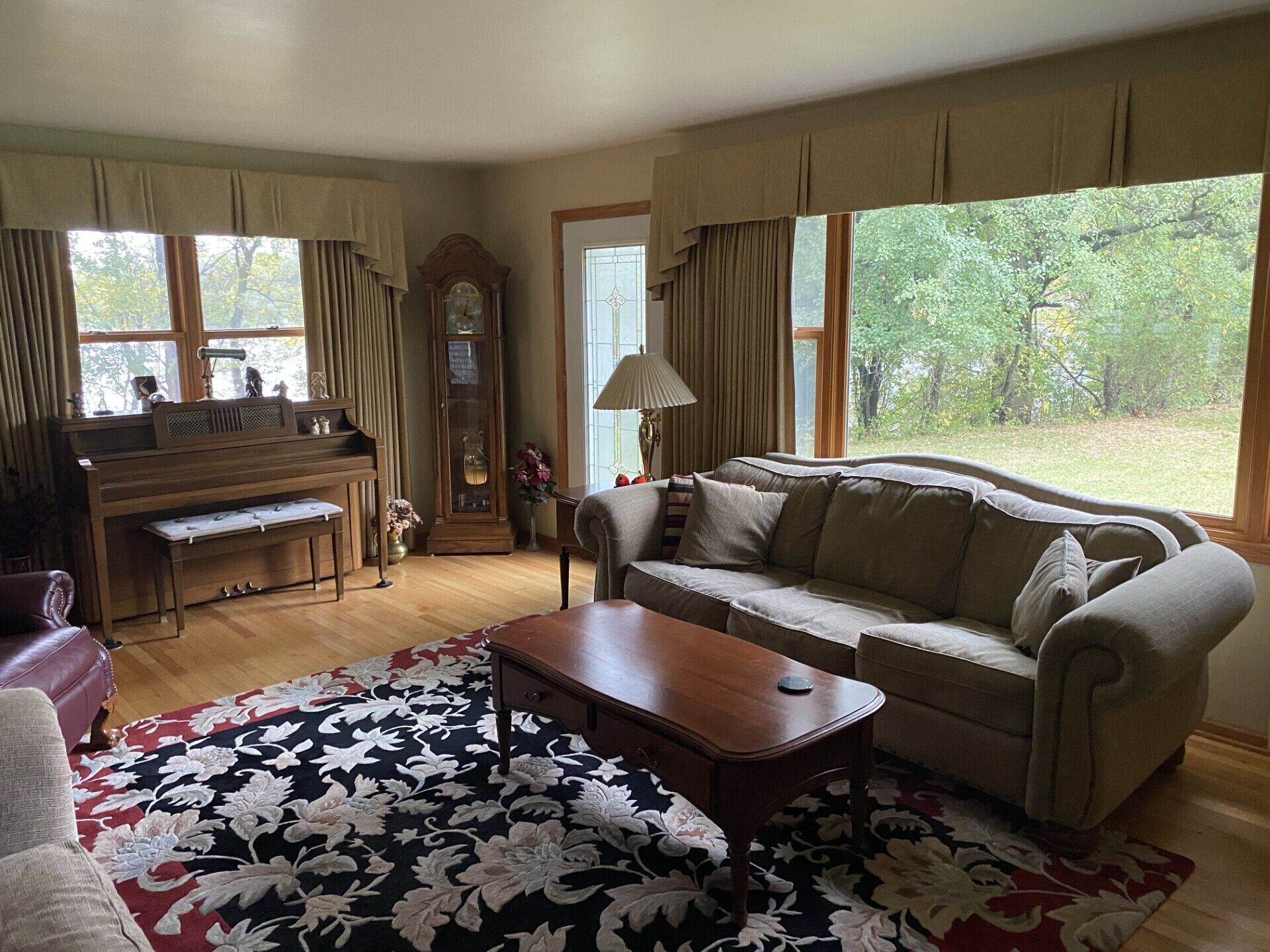 A living room with a piano, a sofa, a coffee table, and a large window with a view of trees.