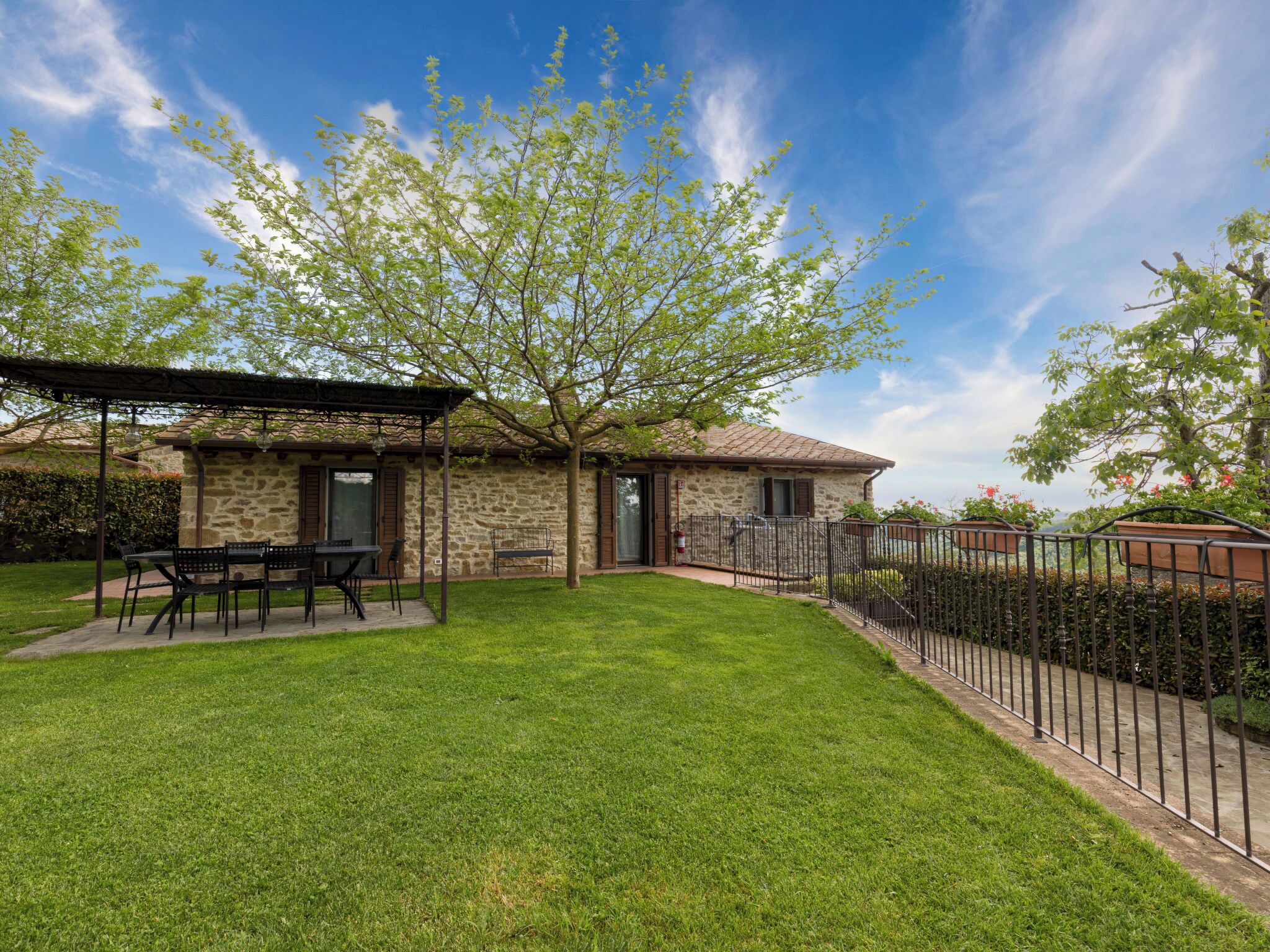 A stone house with a patio, a tree, and a metal fence.