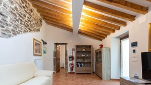 Un espacio habitable amplio con un sofá blanco, vigas de madera, una pared de piedra y suelo de baldosas.