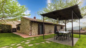 Un edificio de piedra con un porche cubierto, mobiliario exterior y vistas al paisaje.