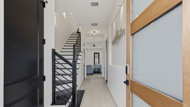 Un couloir moderne avec un escalier, une porte dotée d’un cadre en bois et un luminaire fixé au mur.