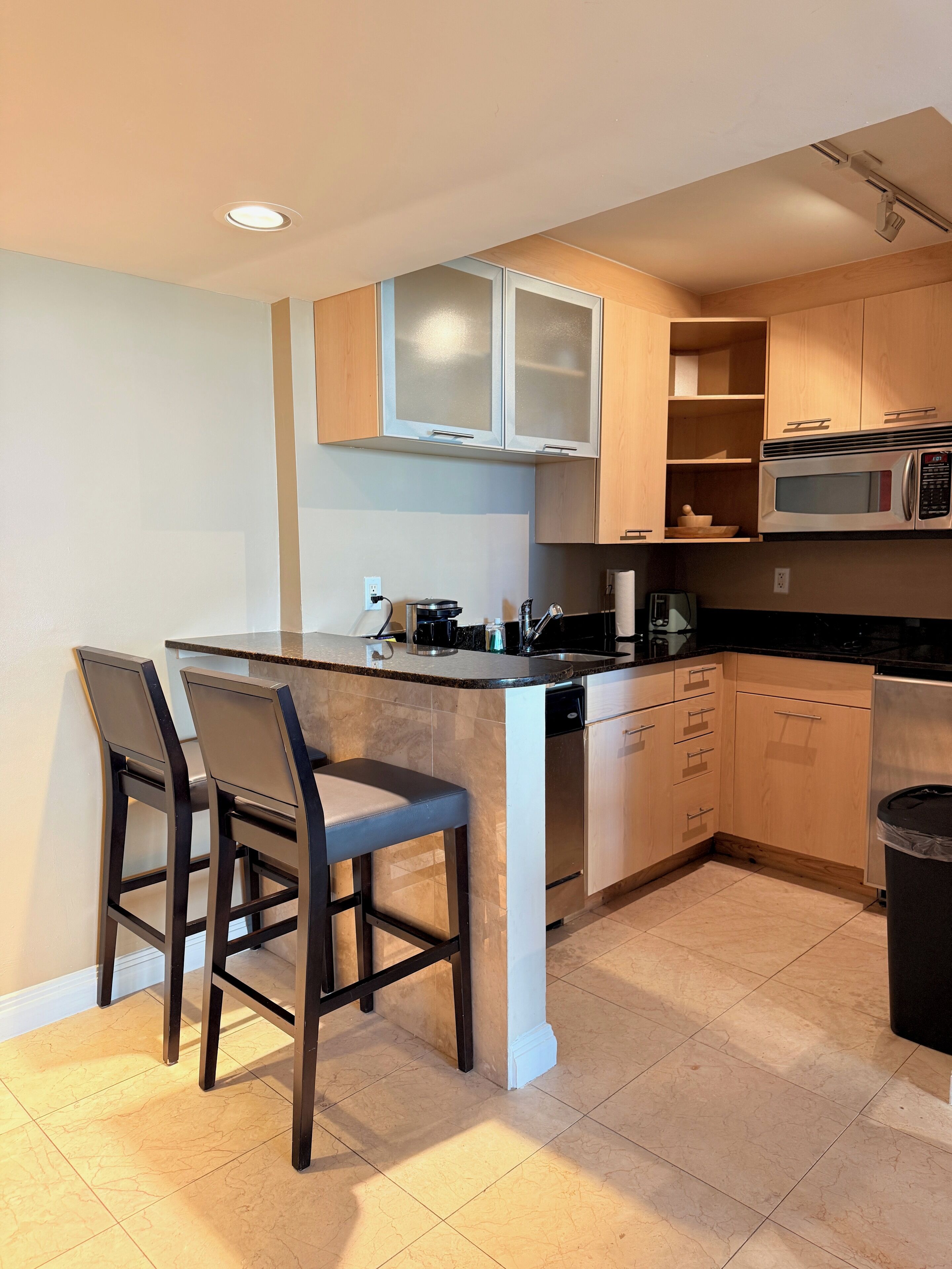 A modern kitchen with a central island, bar stools, wooden cabinets, a microwave, and a dishwasher.