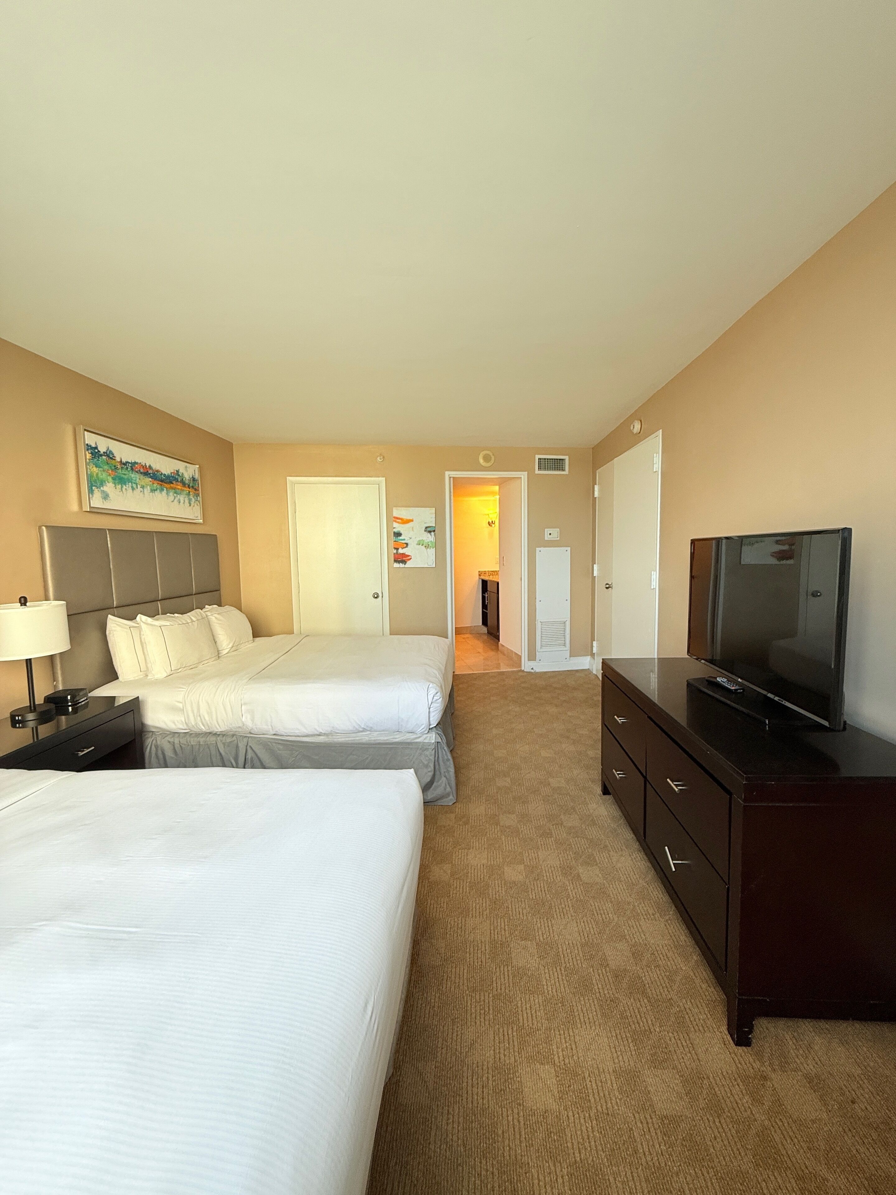 A hotel room with two beds, a TV, a dresser, and a painting on the wall.