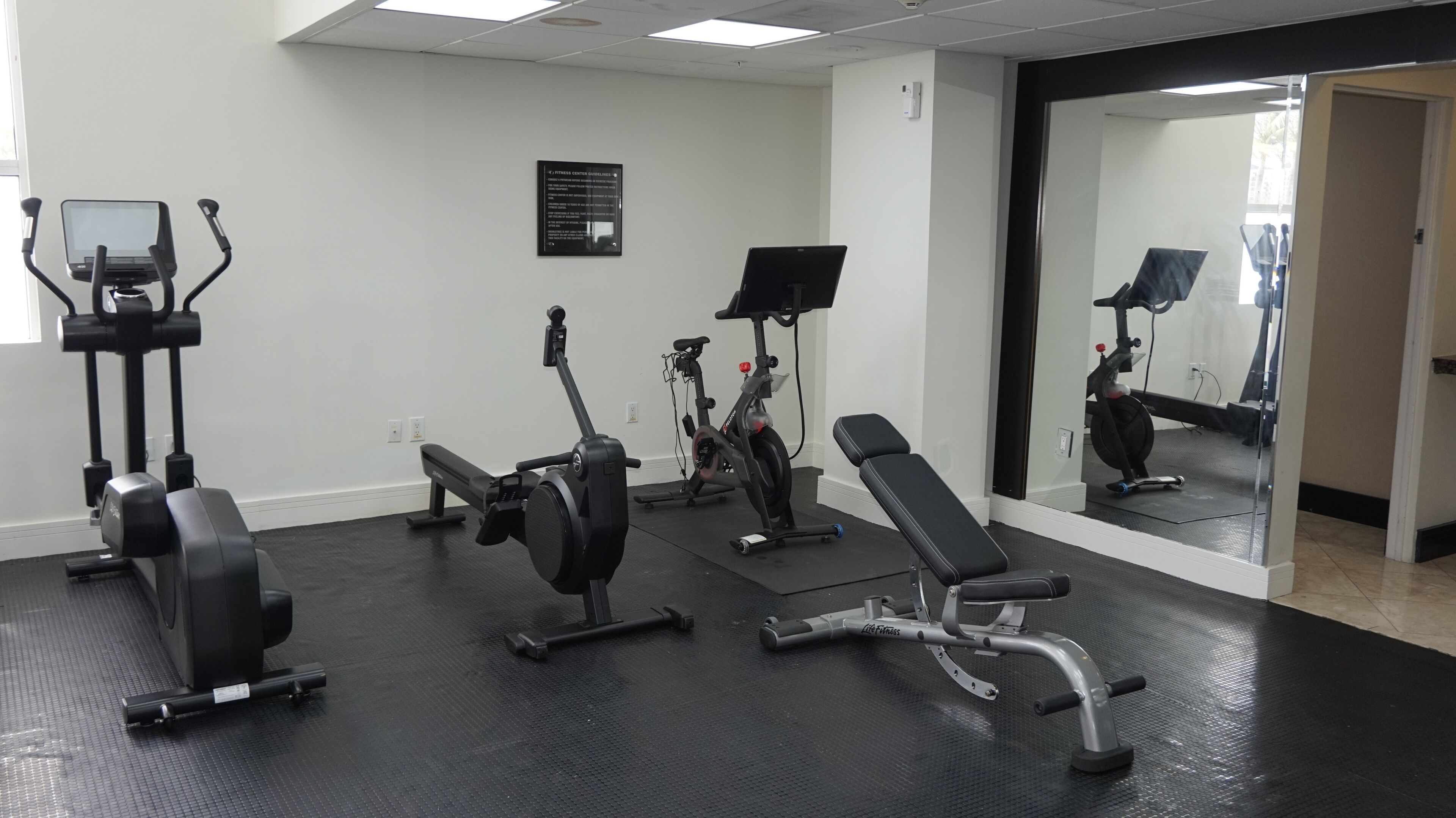 A gym with exercise equipment, a bench, and a mirror.