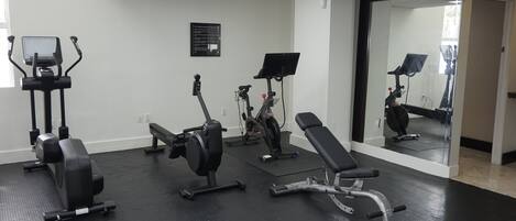A gym with exercise equipment, a bench, and a mirror.