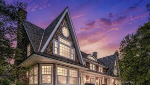 A large, modern house with a steeply pitched roof, multiple windows, and a prominent clock tower. - 6 bed 6 bath cottage on Lake Joseph (Port Carling)