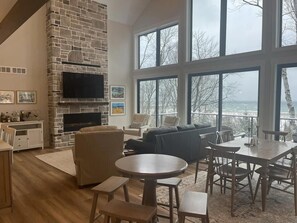 Un salón amplio con chimenea de piedra, una gran mesa de comedor y vistas al exterior a través de amplias ventanas.