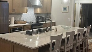 A modern kitchen with wooden cabinets, a central island with bar stools, stainless steel appliances, and pendant lighting. - Lanes End: Spacious Lakefront Retreat in Scenic Grand Marais (Grand Marais)