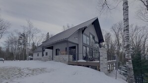 A modern two-story house with a stone foundation, large windows, and a covered porch. - Lanes End: Spacious Lakefront Retreat in Scenic Grand Marais (Grand Marais)