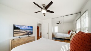 A bedroom with a large bed, a ceiling fan, a television on a wooden dresser, and a view of the beach through the window. - Little Italy Delight! 3 bedroom, backyard, parking (San Diego)