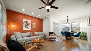 A spacious living room with a gray sofa, a round coffee table, and a dining area with blue chairs. - Little Italy Delight! 3 bedroom, backyard, parking (San Diego)