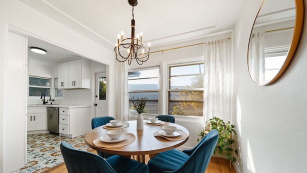 A modern kitchen with white cabinets, a dining table set for six, and a chandelier. - Little Italy Delight! 3 bedroom, backyard, parking (San Diego)