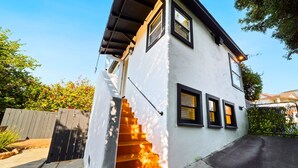 A two-story house with a white exterior, a black roof, and a set of stairs leading to the entrance. - Little Italy Delight! 3 bedroom, backyard, parking (San Diego)