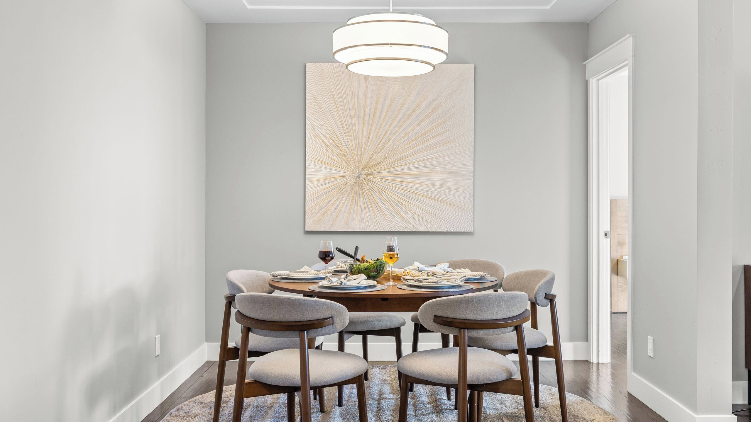 A dining area with a round table, six chairs, and a large abstract painting on the wall.