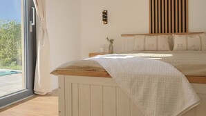 A bedroom with a large window, a bed with a wooden headboard, and a small bedside table with a vase. - Villa in Paradise With Heated Pool (Sveta Nedelja)