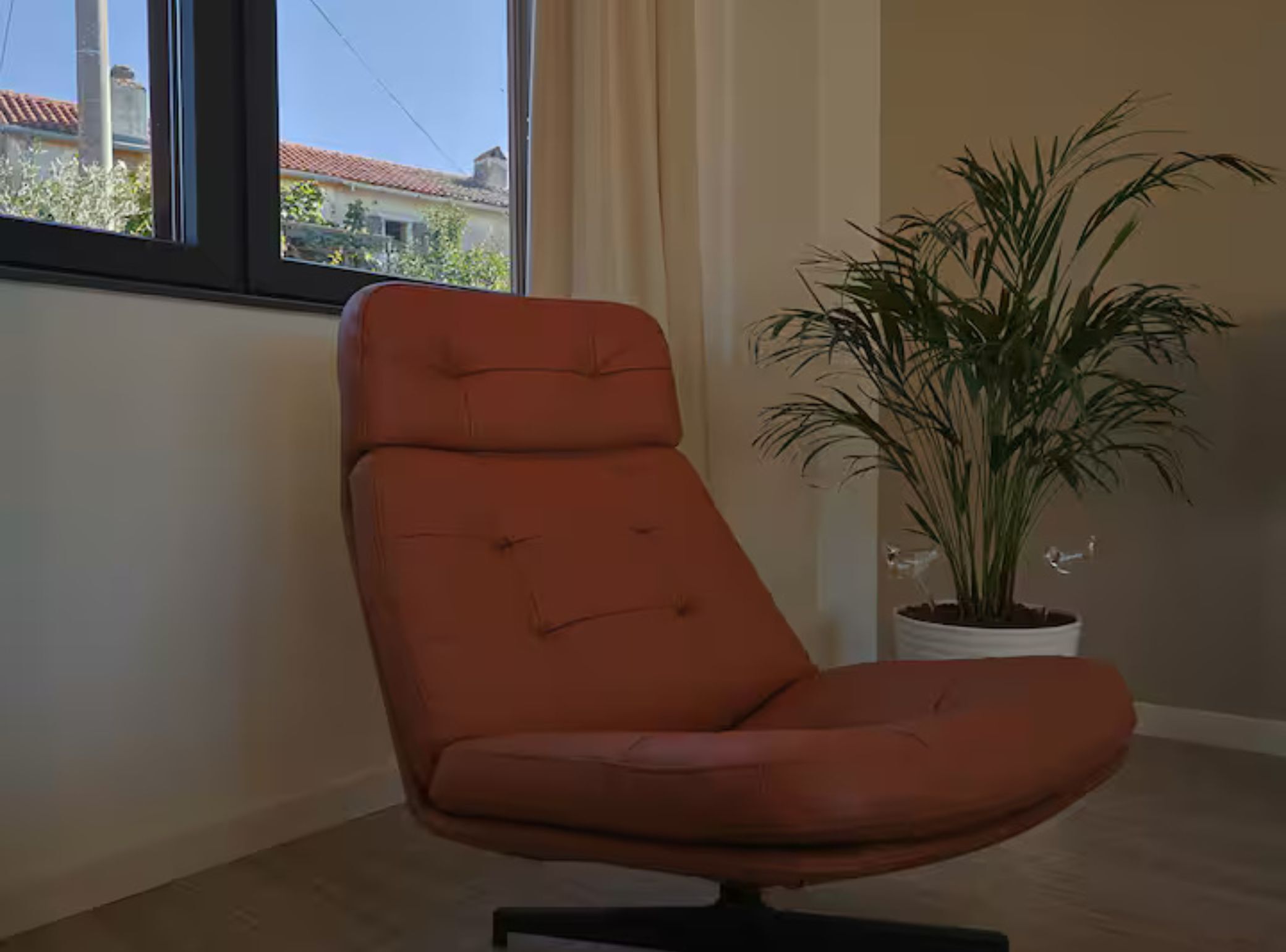 Ein moderner, orangefarbener Sessel mit gepolstertem Sitz und Rückenlehne, platziert in einem Zimmer mit großem Fenster und einem Blumentopf.