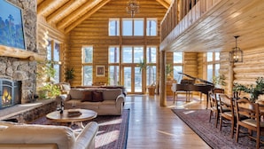 A spacious log cabin interior with a fireplace, a piano, and a large window overlooking a snowy landscape. - Sleeps 20, Secluded 7bdr Retreat on 71 Priv Acres Elkstone Lodge by Avantstay (Glenwood Springs)