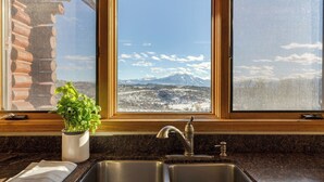 A kitchen with a granite countertop, stainless steel sink, and a window with a view of a snowy mountain range. - Sleeps 20, Secluded 7bdr Retreat on 71 Priv Acres Elkstone Lodge by Avantstay (Glenwood Springs)