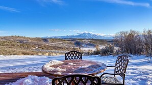 A wooden table and chairs on a snow-covered deck with a view of snow-capped mountains in the background. - Sleeps 20, Secluded 7bdr Retreat on 71 Priv Acres Elkstone Lodge by Avantstay (Glenwood Springs)