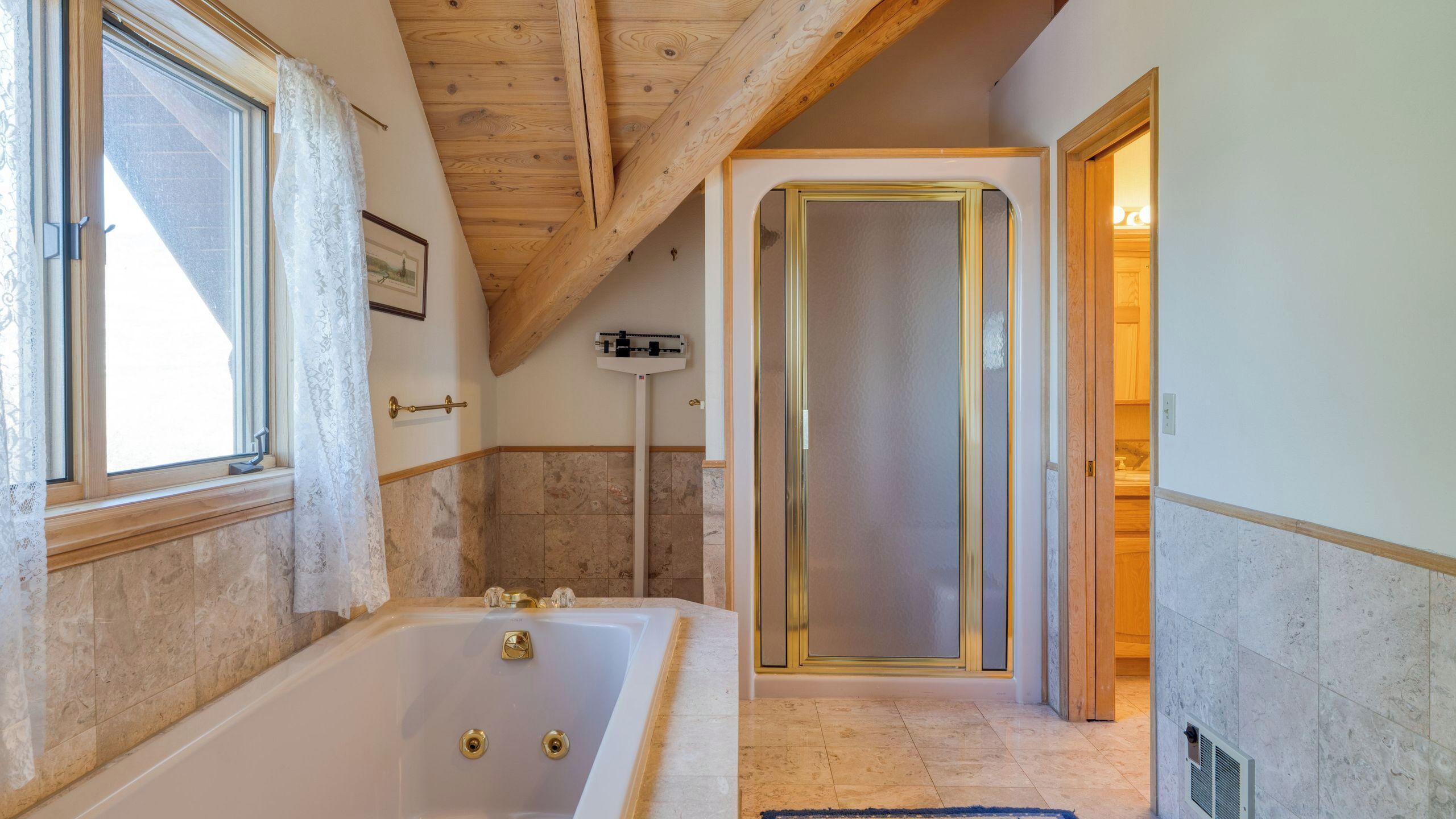 A bathroom with a bathtub, a shower enclosure, and a window with curtains.