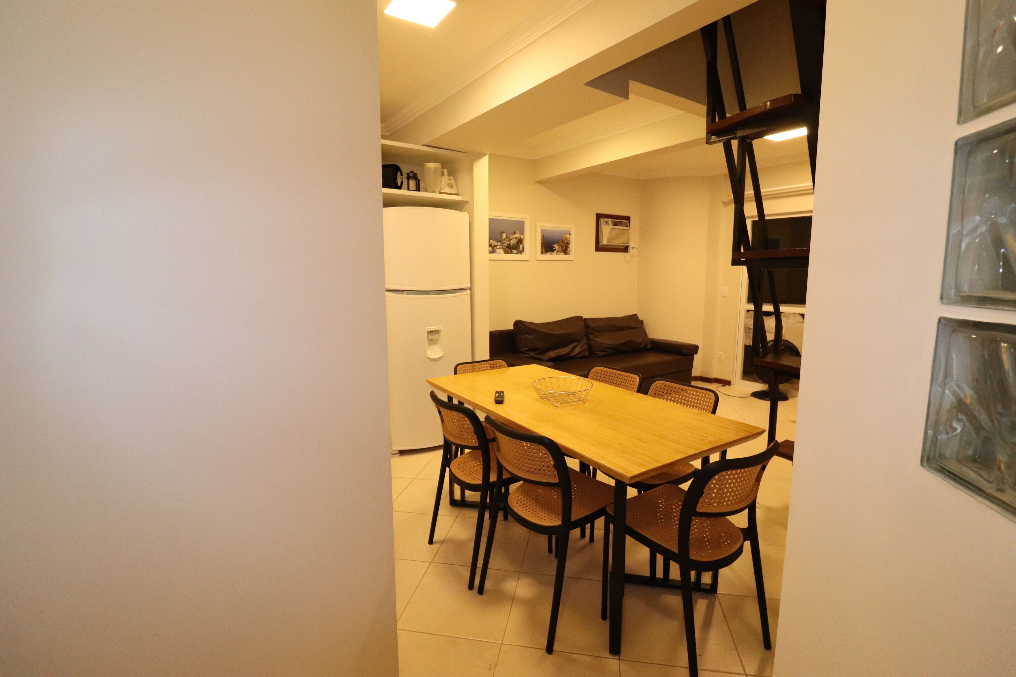 A compact living space with a dining area featuring a wooden table and black chairs, a sofa, and a refrigerator.