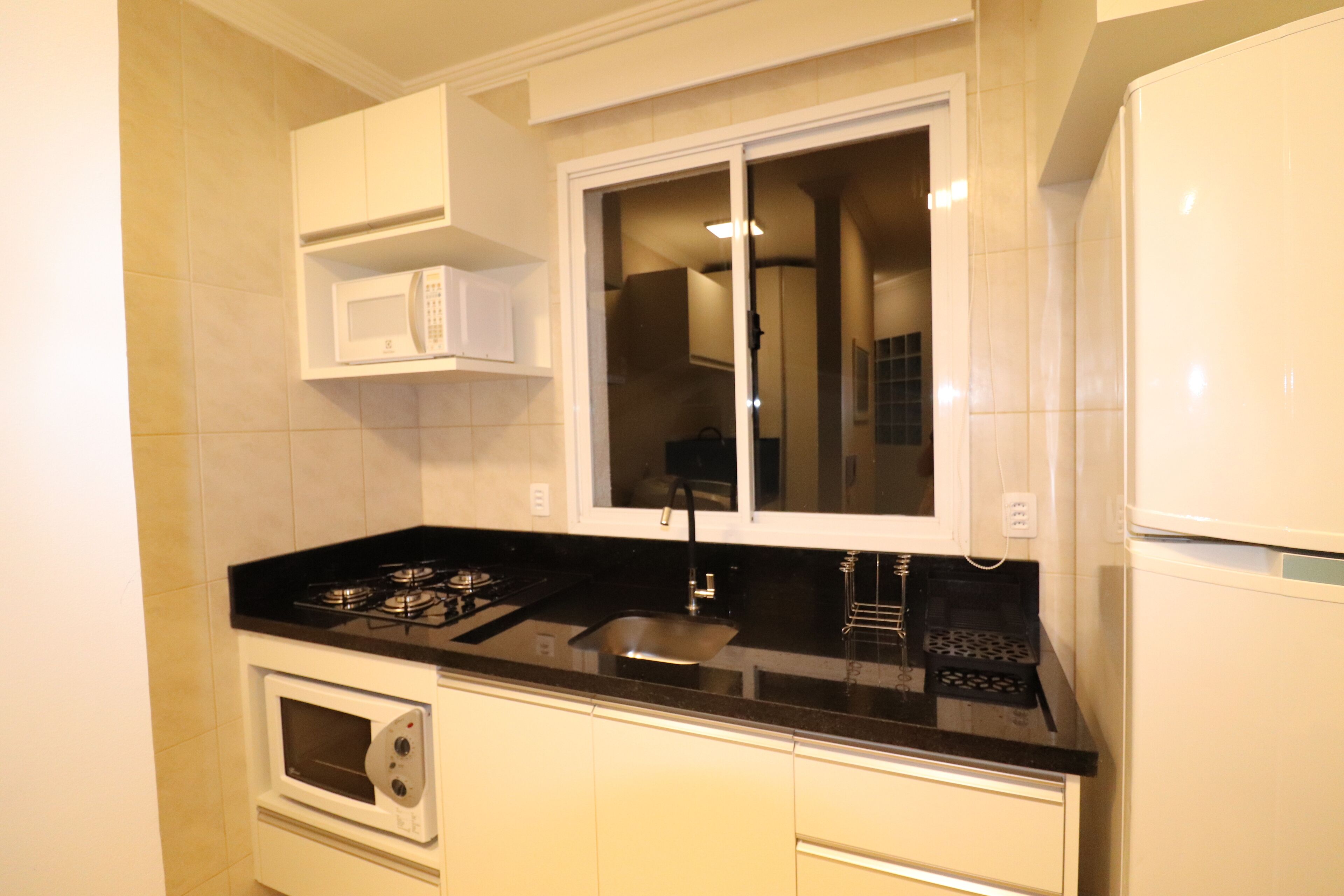 A compact kitchen with a stove, microwave, sink, and white cabinets.