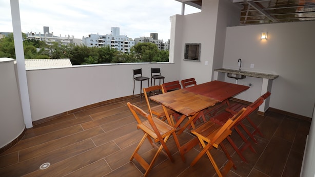 Un comedor con mesa y sillas de madera, una pequeña cocina con pileta, y vistas a edificios y vegetación.