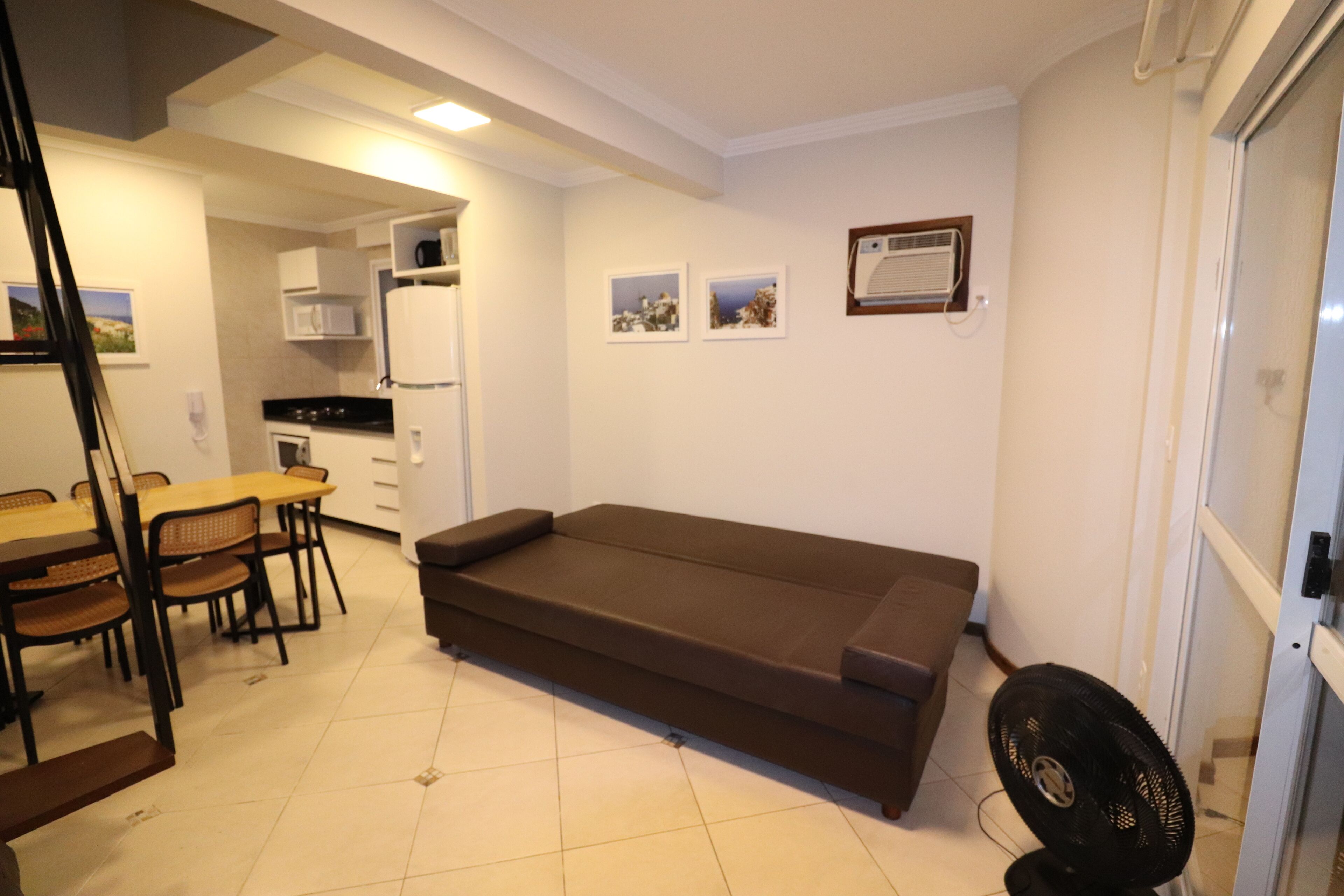 A compact living space with a sofa, dining table, chairs, a kitchenette, and a wall-mounted air conditioner.