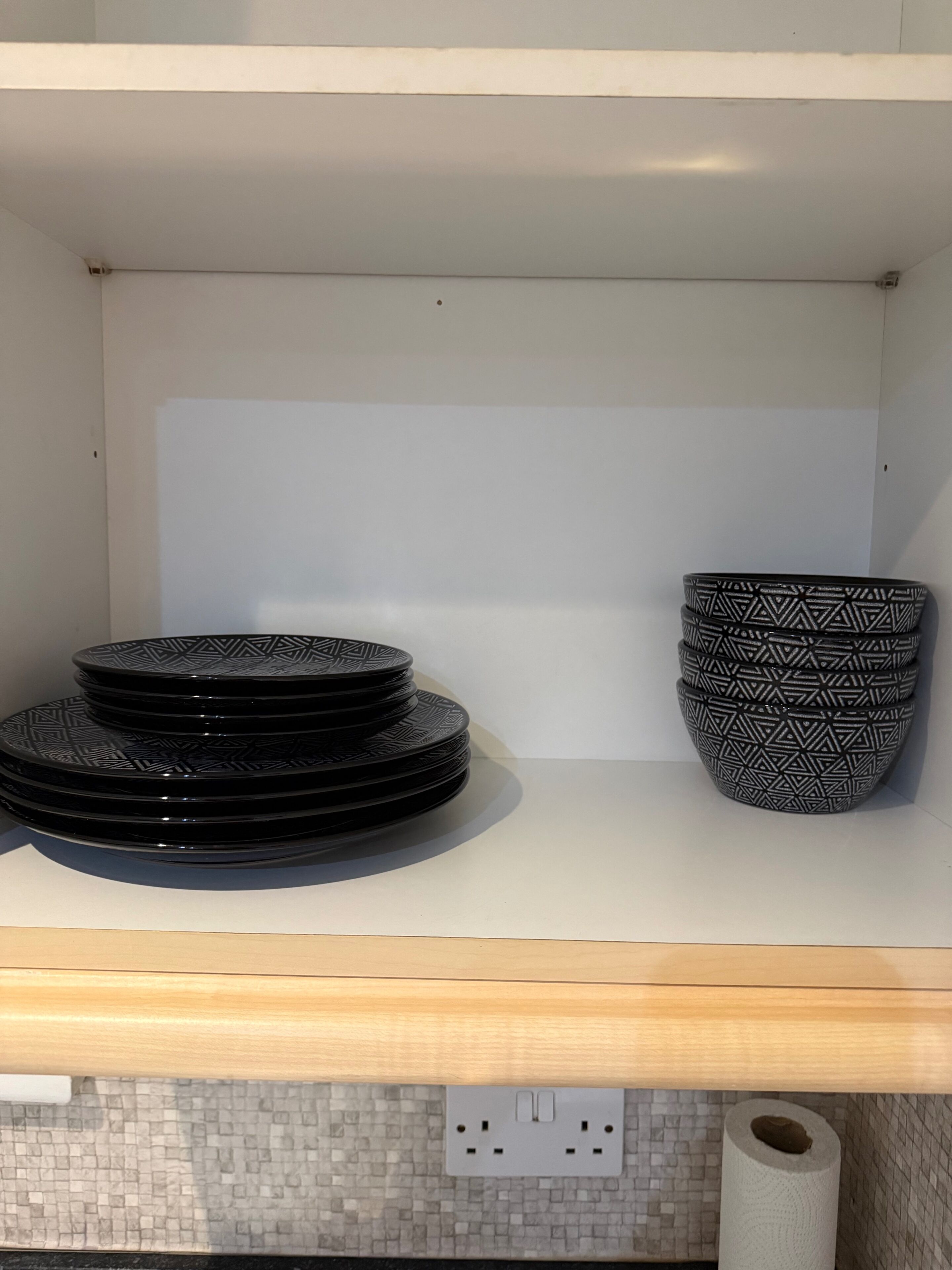 A kitchen shelf with stacked black plates and a single patterned bowl.