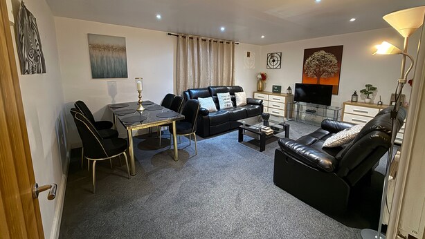 Uma sala de estar moderna com um sofá de couro preto, uma mesa de centro de vidro e uma mesa de jantar com cadeiras.